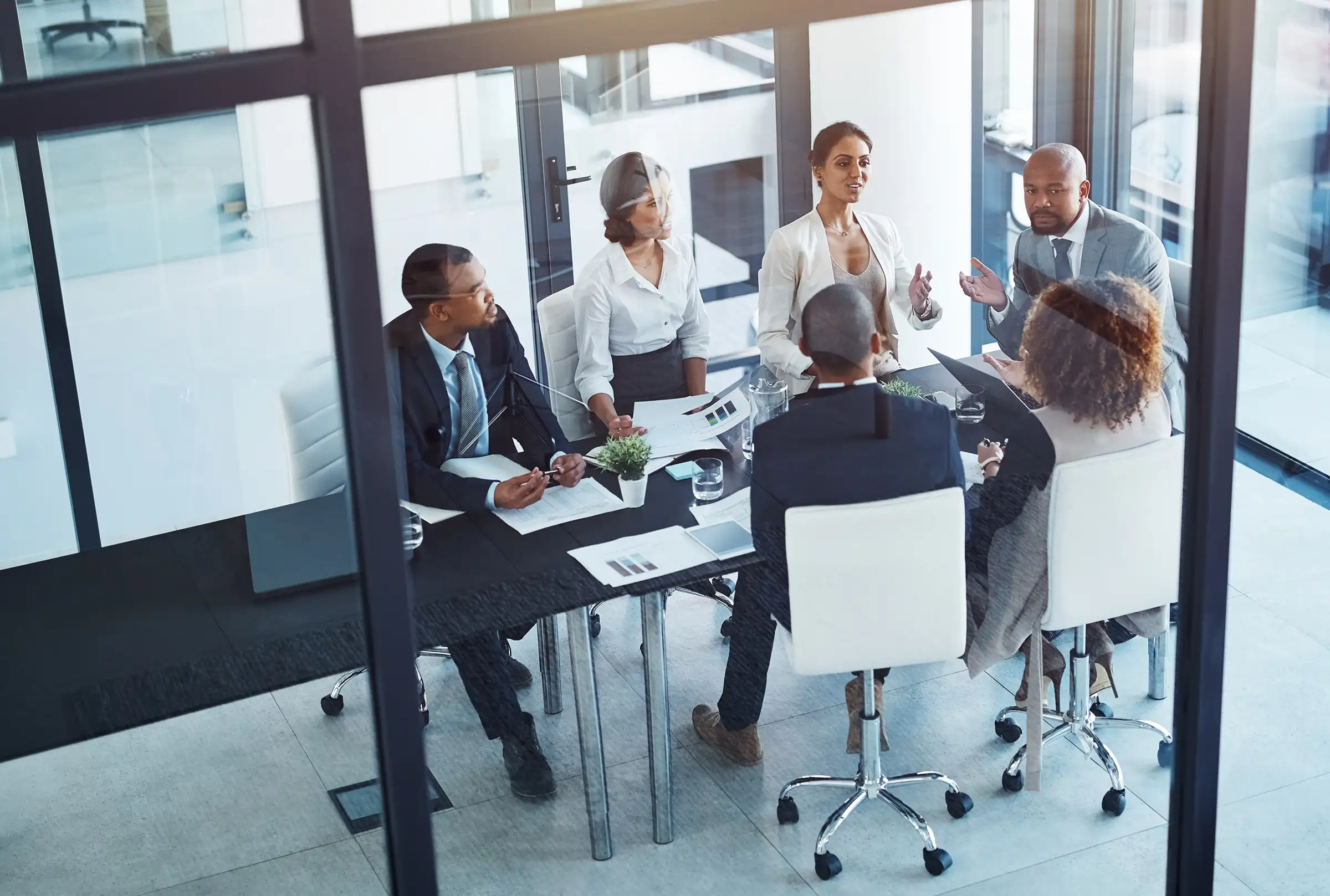 team Colleagues discussing plans around a glass-walled meeting room table